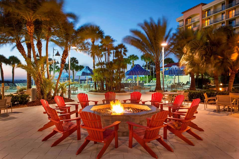 Beachfront fire pit with red Adirondack chairs and palm trees at twilight