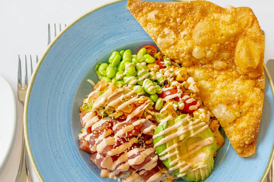 Sushi dish with avocado, crispy wonton, and edamame on blue plate