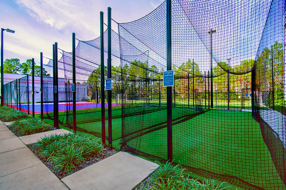 Indoor sports facility with colorful athletic courts enclosed by netting at dusk.