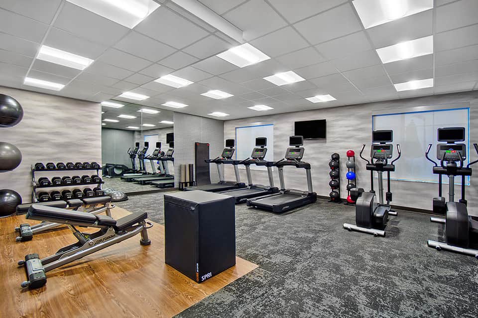 Modern fitness center with treadmills, exercise bikes, weights, and mirrored walls