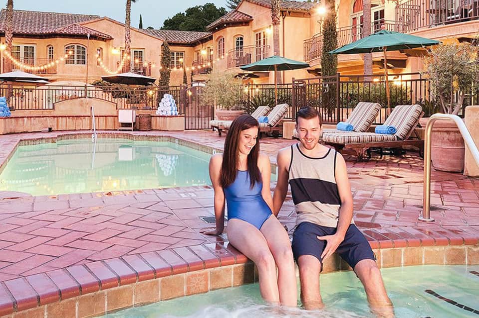 Mediterranean-style resort pool with spa, loungers, terracotta buildings, and evening lighting