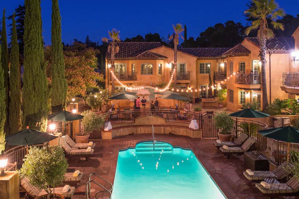 Illuminated courtyard pool at night with Spanish-style architecture, palm trees, and outdoor seating