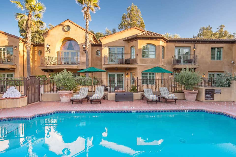 Spanish-style resort building with terra cotta exterior, lounge chairs, turquoise pool, and palm trees