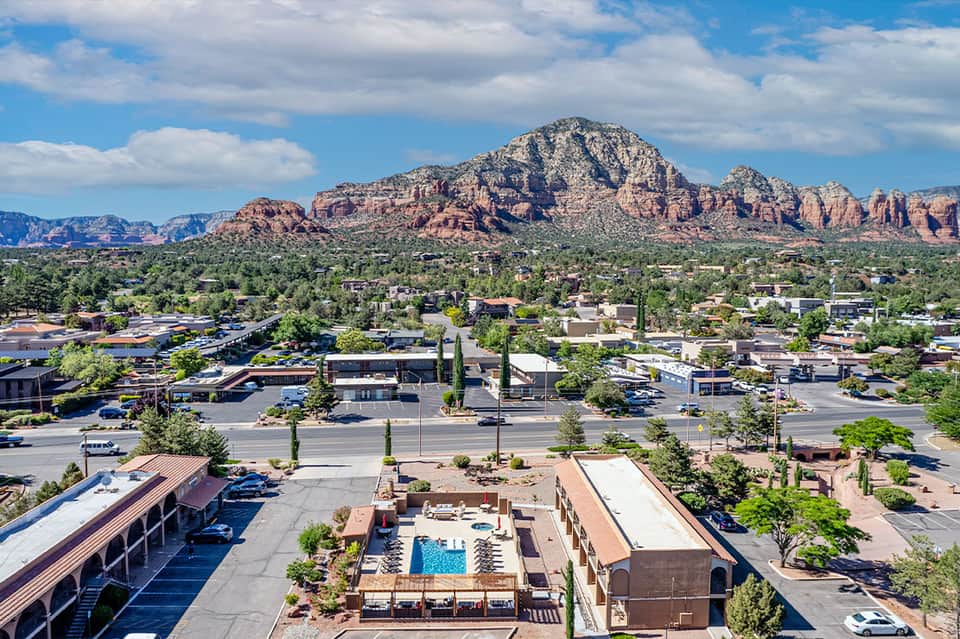 Aerial view of hotel with pool surrounded by town and red rock mountains in background