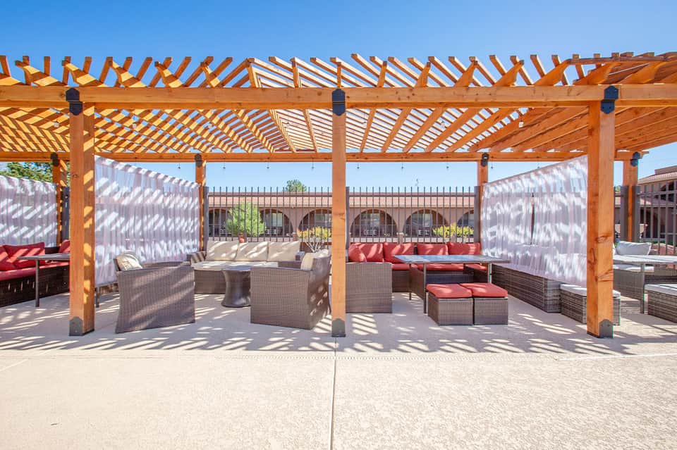 Shaded outdoor terrace with wooden pergolas, woven lounge seating, and red accent cushions