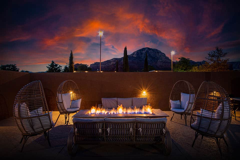 Fire pit seating area at night with woven chairs, mountain backdrop, and dramatic sunset sky