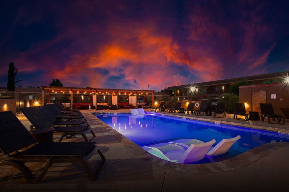 Illuminated resort pool at night with colorful underwater lighting and lounge chairs