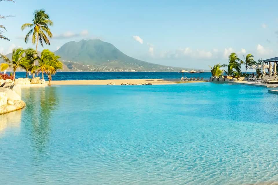 Turquoise lagoon pool with palm trees and volcanic mountain backdrop at tropical beach resort