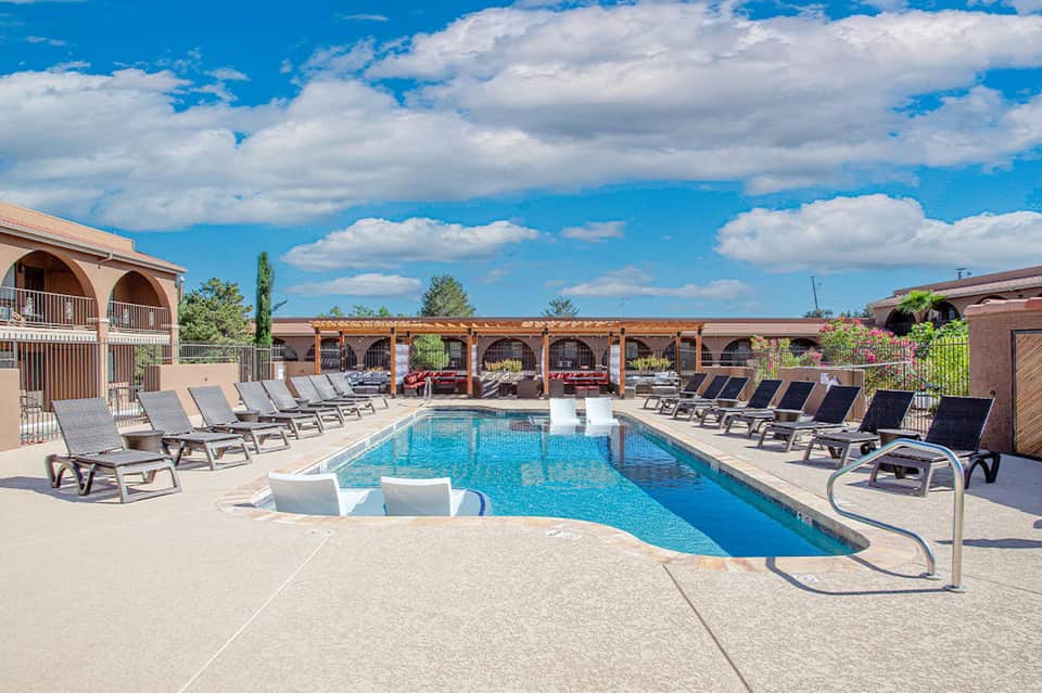 Resort pool with lounge chairs, wooden pergolas, southwestern architecture, blue sky and clouds overhead
