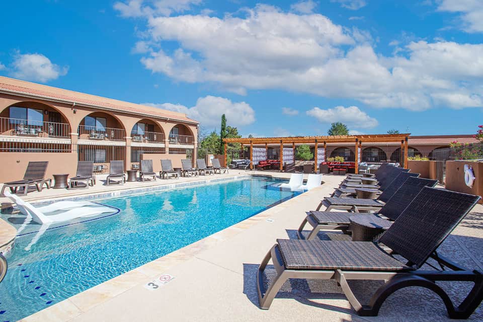 Resort swimming pool with lounge chairs under wooden pergolas and blue sky