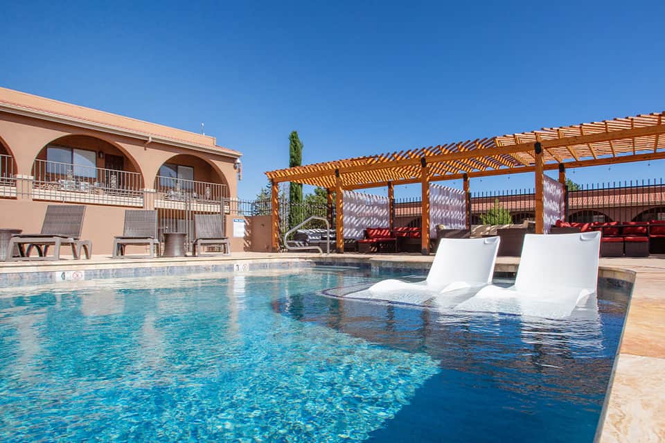 Resort pool with submerged loungers, wooden pergola, and desert mountain landscape