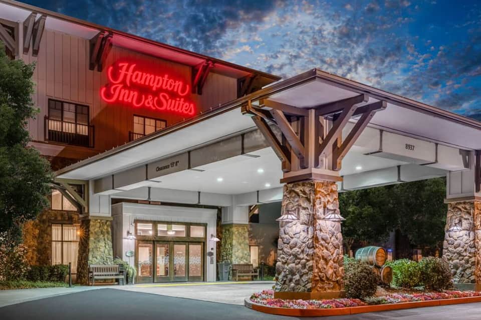Hampton Inn & Suites entrance at dusk with neon sign and wooden architectural details