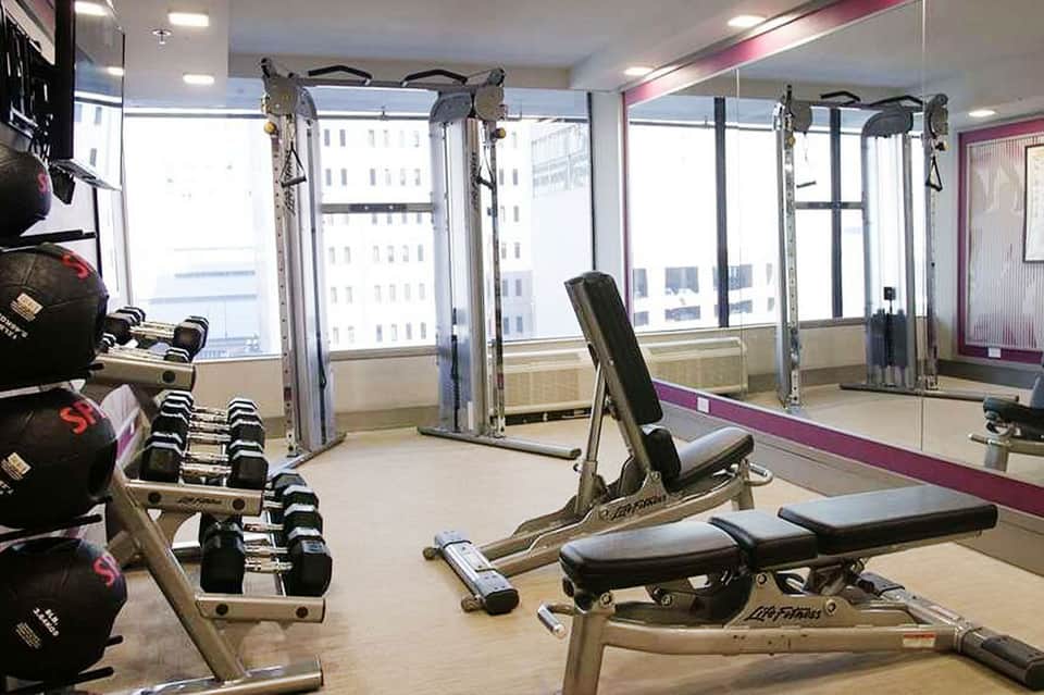 High-rise fitness center with dumbbells, weight machines, mirrors, and city views through windows