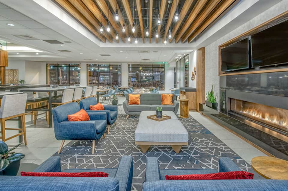 Contemporary hotel lounge with wooden ceiling, blue armchairs, fireplace, and floor-to-ceiling windows