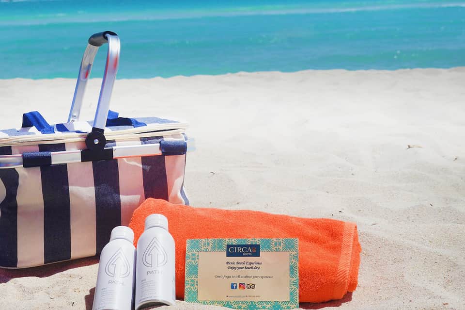 Beach picnic setup with striped basket, orange towel, sunscreen bottles, and turquoise ocean backdrop
