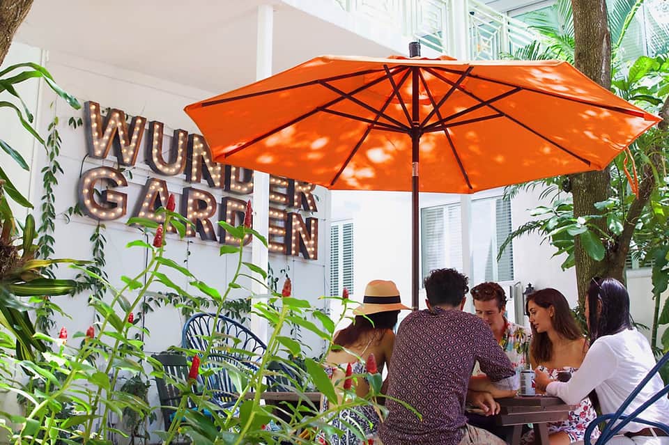 Outdoor garden dining area under orange umbrella with group of guests and lush tropical plants
