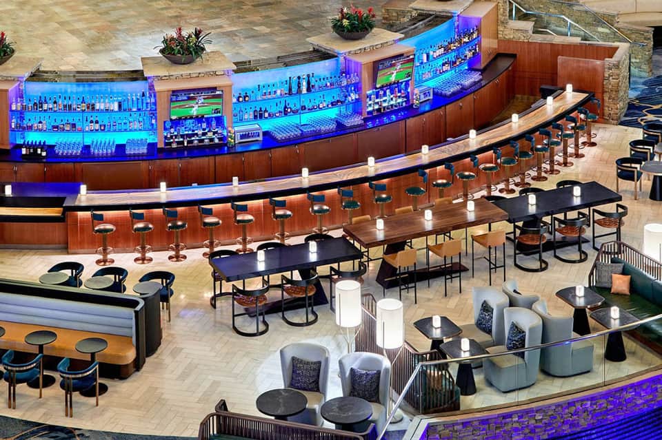 Modern resort bar with curved blue-lit shelving, wooden counter, and multiple bar seating sections