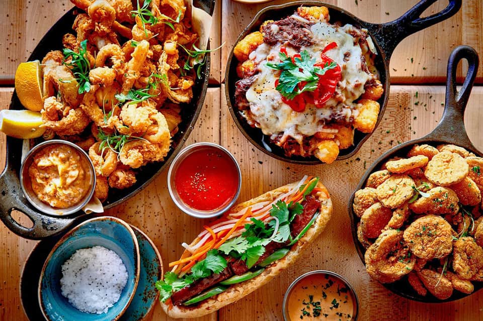 Cast iron skillet appetizers including shrimp, croquettes, pizza and dipping sauces on wooden table