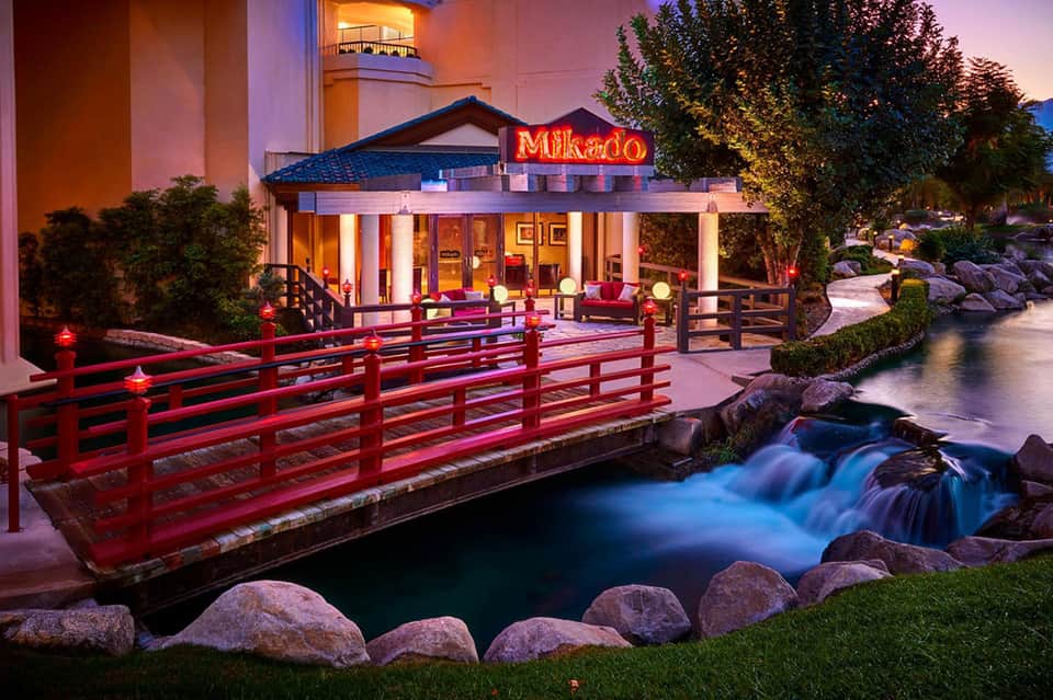 Illuminated Japanese-style restaurant entrance with red bridge over flowing water at dusk