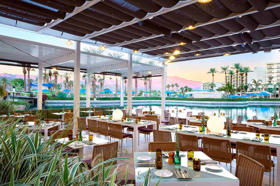 Upscale outdoor dining area under pergola with mountain and water views at dusk