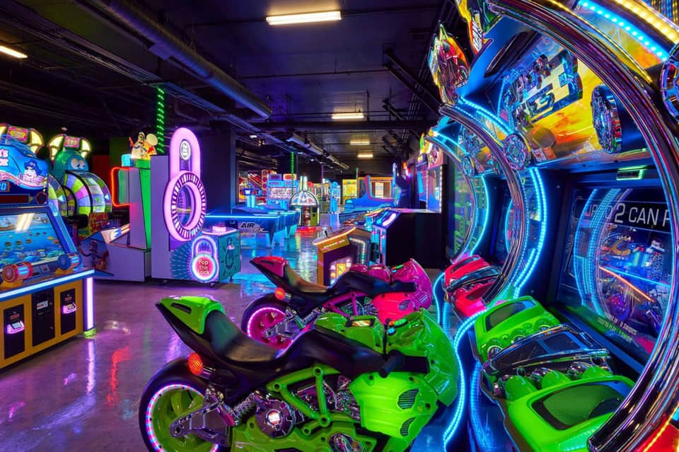 Vibrant arcade game room with neon-lit racing bikes, vintage games, and colorful lighting