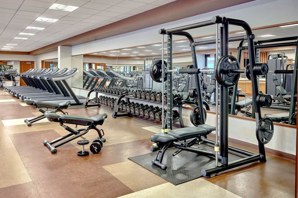 Modern fitness center with rows of cardio equipment, dumbbells, weight racks, and mirrored walls