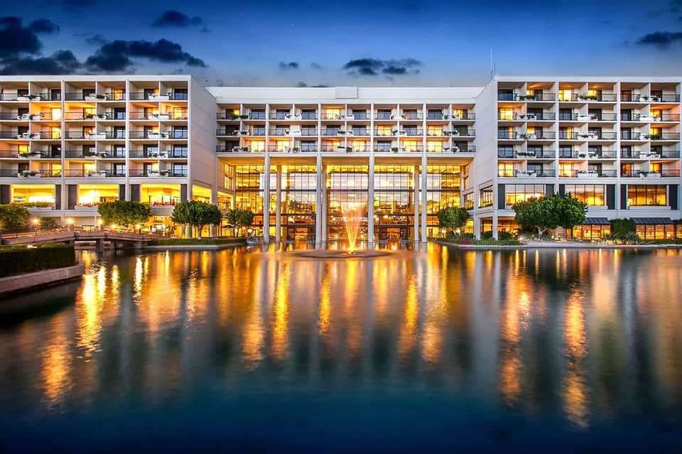 Modern waterfront hotel building at dusk with illuminated windows reflected in water