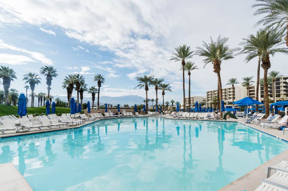 Large rectangular pool with blue umbrellas, palm trees, and mountain views