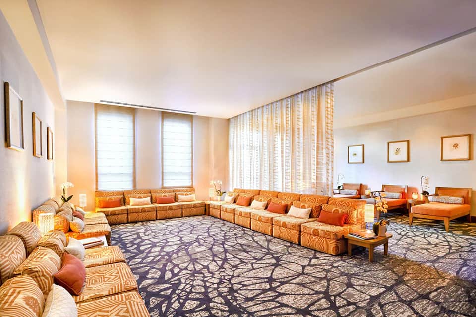 Elegant hotel lounge with sectional seating, orange upholstery, large windows, and contemporary decor