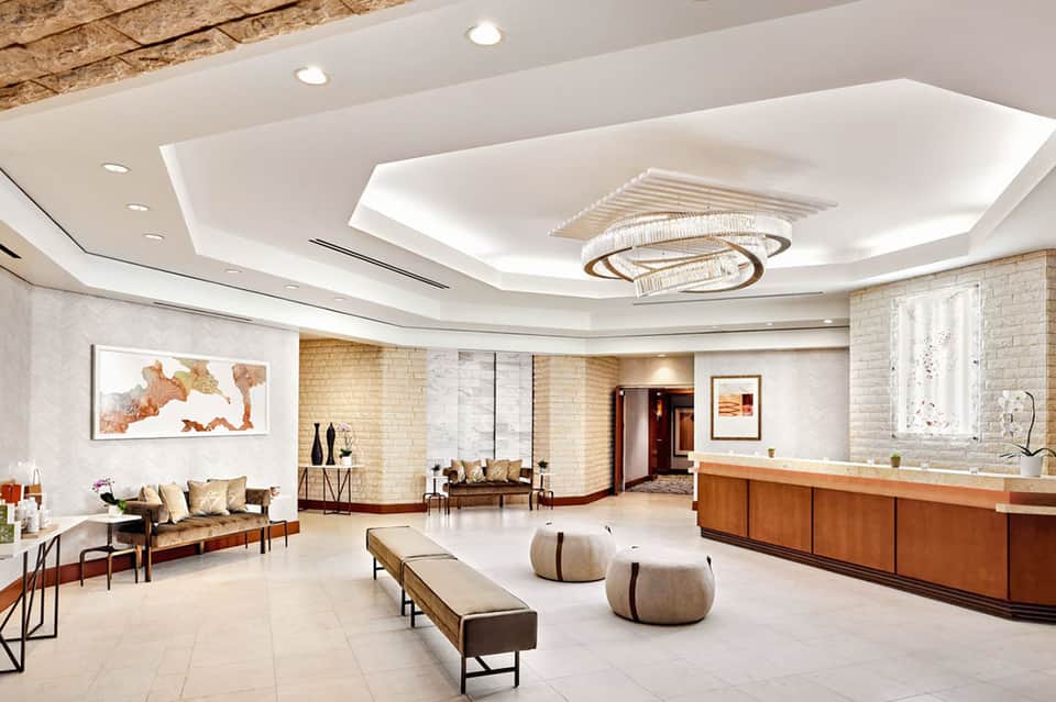 Modern hotel lobby with curved white ceiling, recessed lighting, wooden reception desk, and seating area