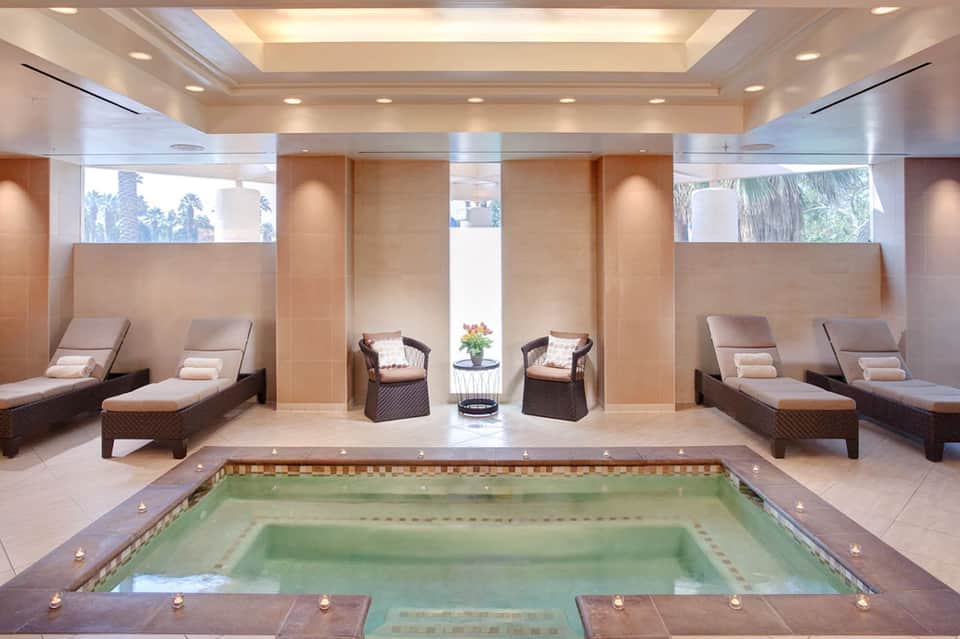 Indoor spa pool surrounded by lounge chairs, columns, and high ceiling with natural light