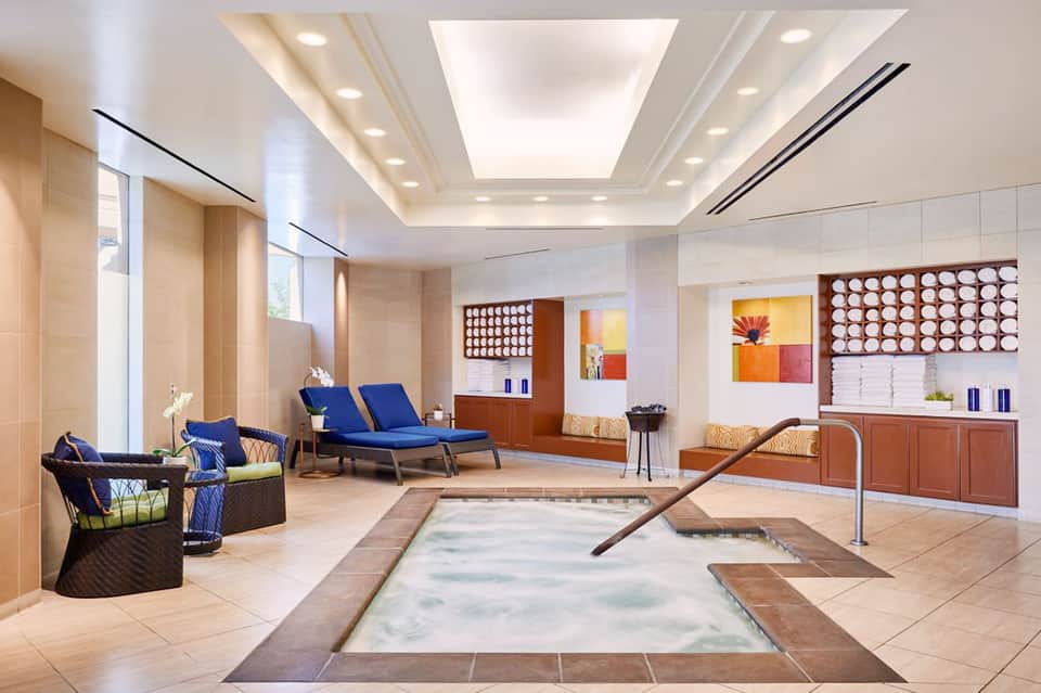 Spa indoor pool with whirlpool jets, lounging area, blue seating and modern architectural ceiling