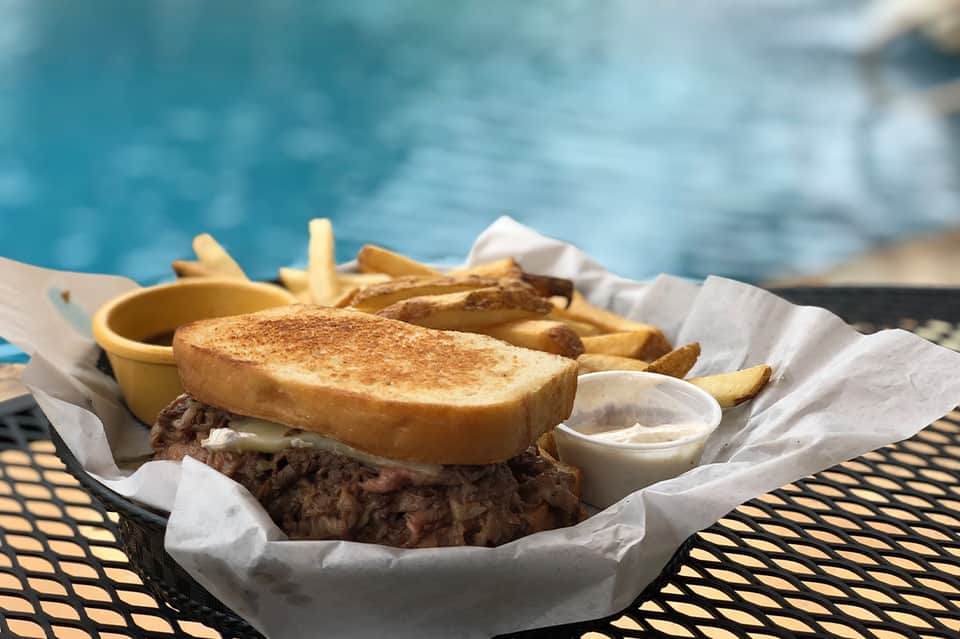 Poolside sandwich and French fries served in paper wrapper with ocean view background
