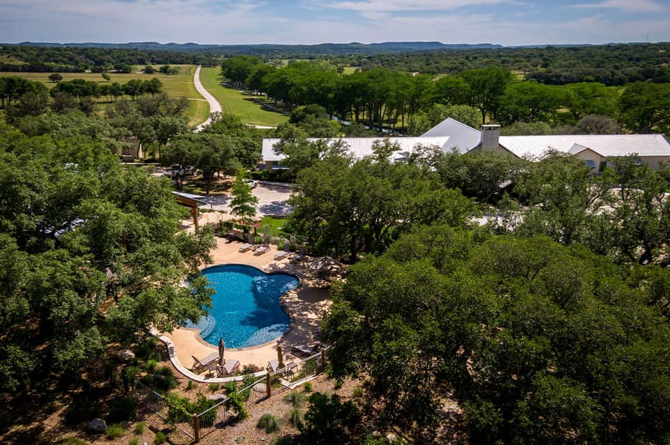 Aerial view of luxury resort pool nestled in trees with white buildings and river