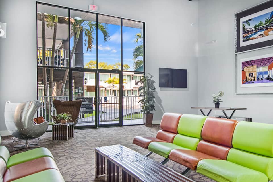 Modern lobby lounge with alternating pink and green seating, large windows overlooking tropical courtyard area