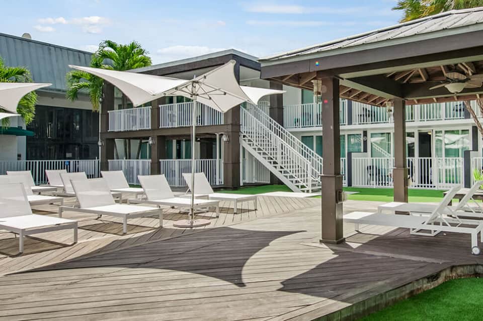 Modern resort deck with lounge chairs, white sail shade, covered pavilion, and multi-level architecture