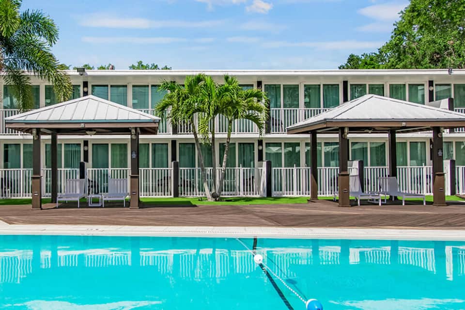 Olympic-sized swimming pool with covered pavilions, white railings, and modern building with palm trees