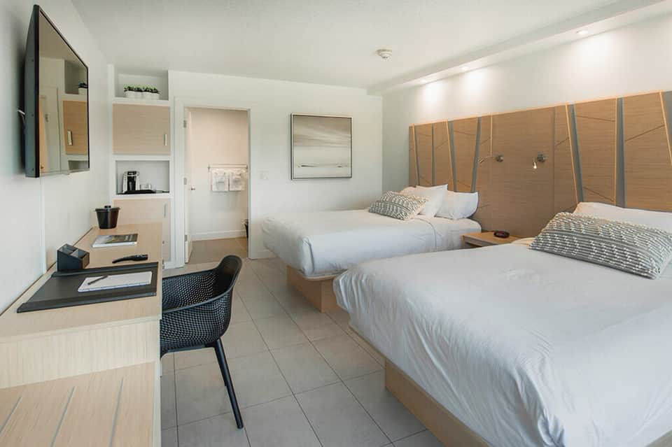Modern hotel room with two queen beds, desk, and neutral wood and white furnishings