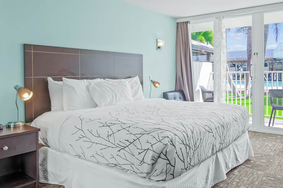 Beachfront hotel bedroom with turquoise walls, white bedding, and ocean view from balcony with glass doors