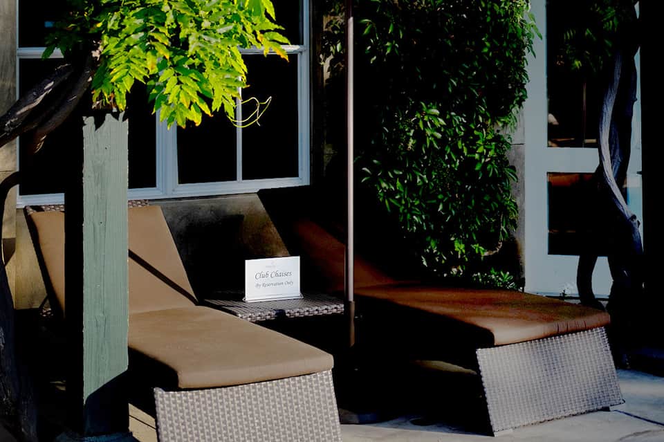 Outdoor seating area with woven chairs under pergola surrounded by lush green foliage