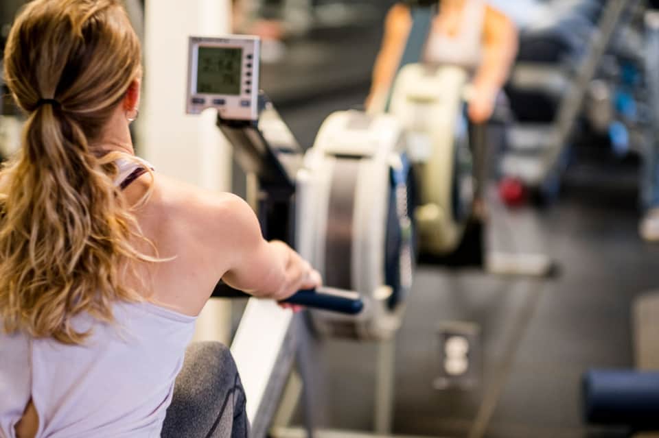 Woman exercising on rowing machine at modern hotel fitness center gym