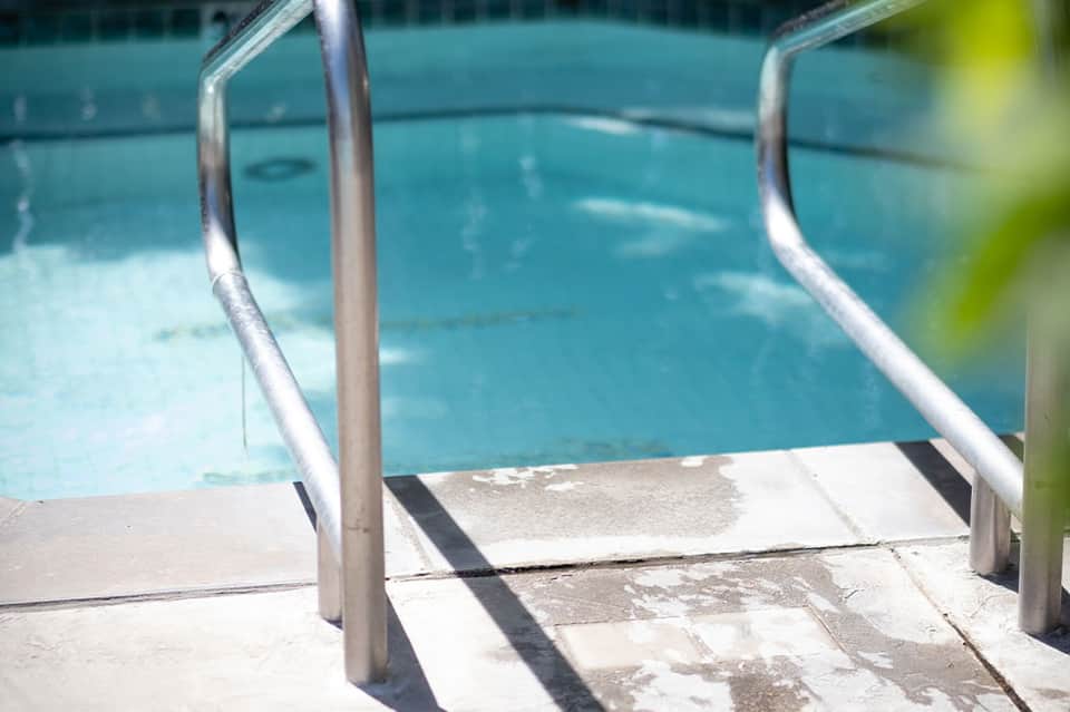 Swimming pool access with chrome handrails and concrete deck stairs