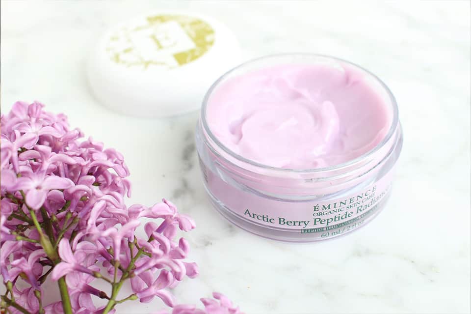 Pink Arctic Berry Peptide skincare cream jar next to fresh purple flowers on white background