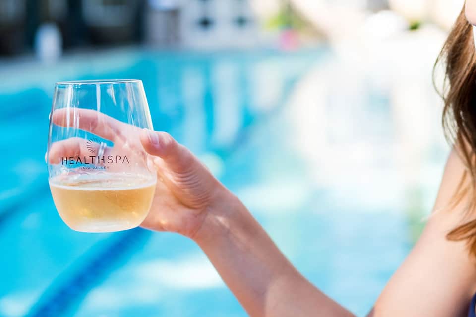 Guest holding branded wine glass with pool and resort grounds blurred in background