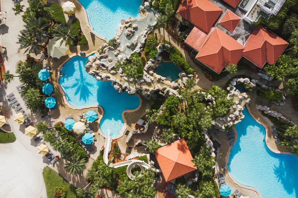 Aerial view of resort with multiple turquoise pools, tropical landscaping, orange umbrellas, and interconnected courtyards