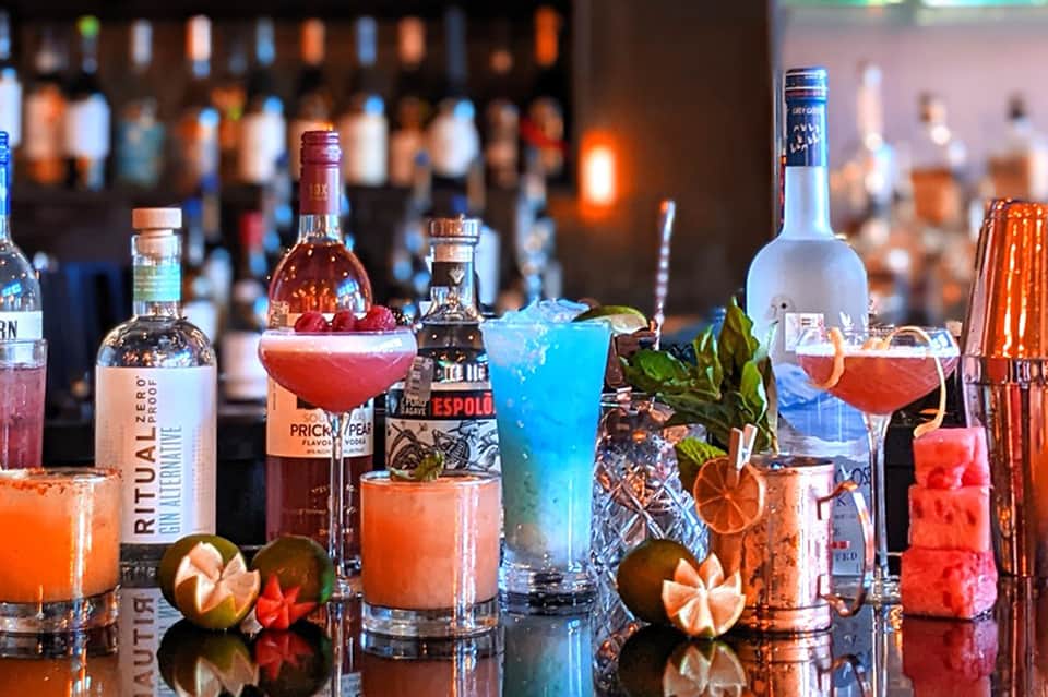 Colorful cocktails at resort bar with spirits bottles, tropical garnishes, and ambient lighting