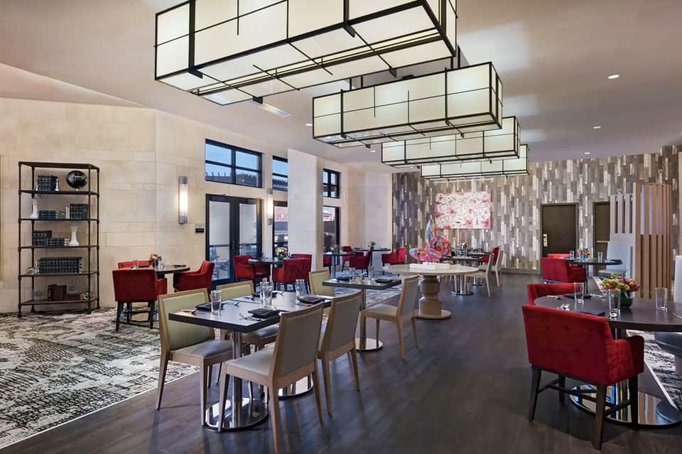Contemporary restaurant interior with red chairs, geometric ceiling fixtures, and floral artwork