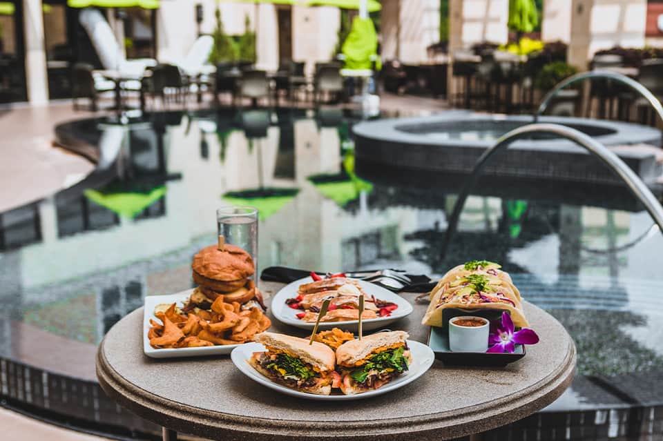 Resort poolside dining table with burgers, appetizers, and water glasses overlooking hot tubs