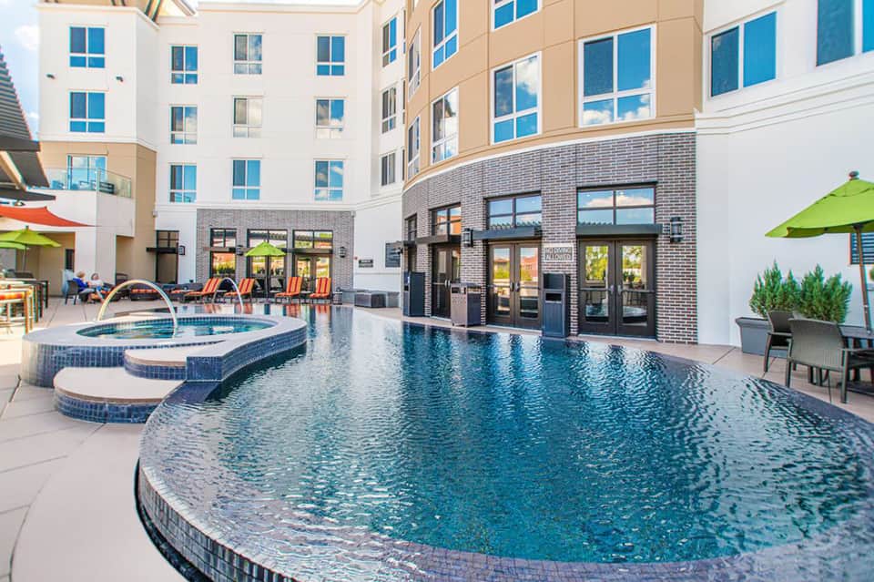 Modern courtyard pool with blue spa jets, colorful lounge chairs, and residential building