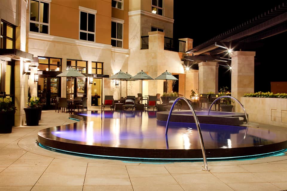 Elegant nighttime courtyard with illuminated round spa pool, seating areas, and architectural columns